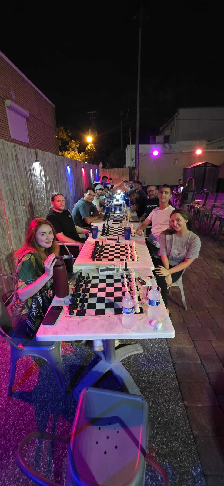 The first league night of season 10: three long tables of boards on the patio at Kava Social Club, sixteen players under the string lights