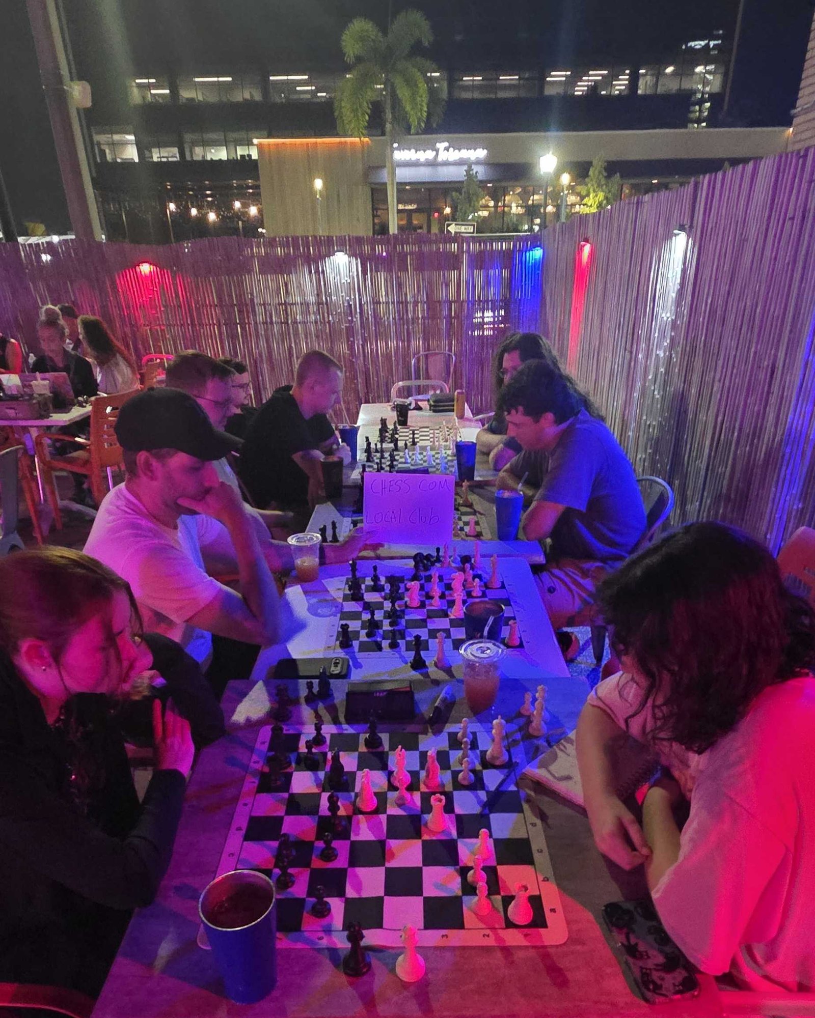 Jugadores en las mesas del patio de Kava Social Club en una noche de estudio de martes, partidas en curso bajo el neón