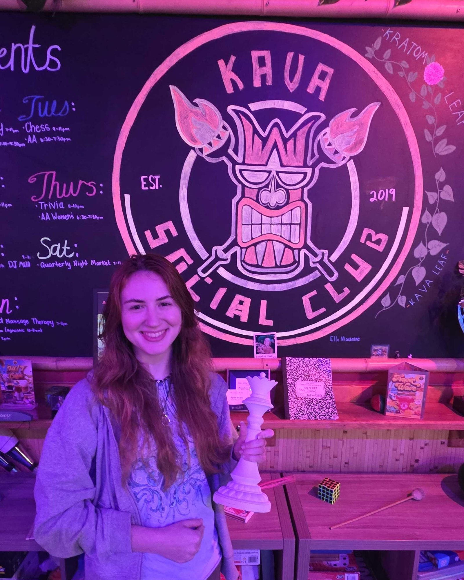 Maddie holding the white queen trophy for Best Female Player in front of the Kava Social Club sign