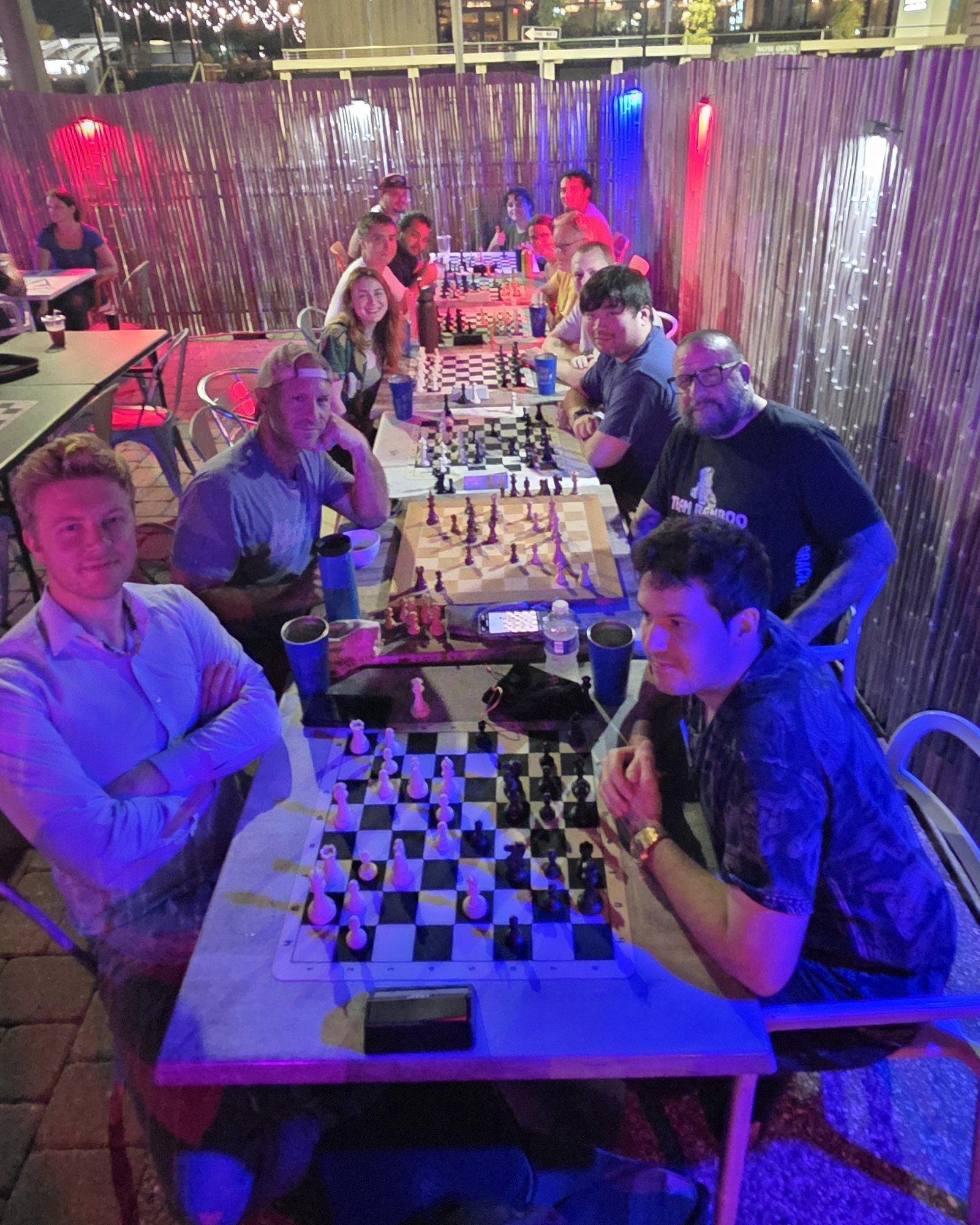 Players along the long table on the back patio at Kava Social, looking up from their games under red and blue lights