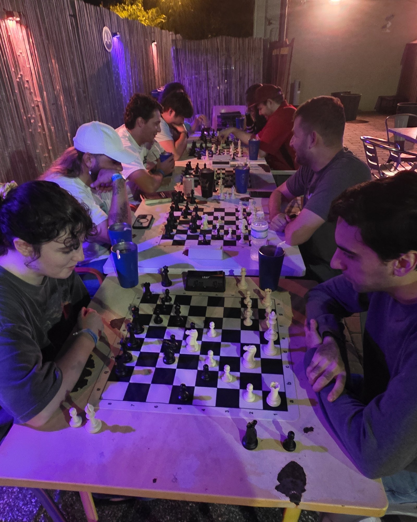 Players at the long tables on the back patio at Kava Social on a Tuesday study night, under purple and red lights